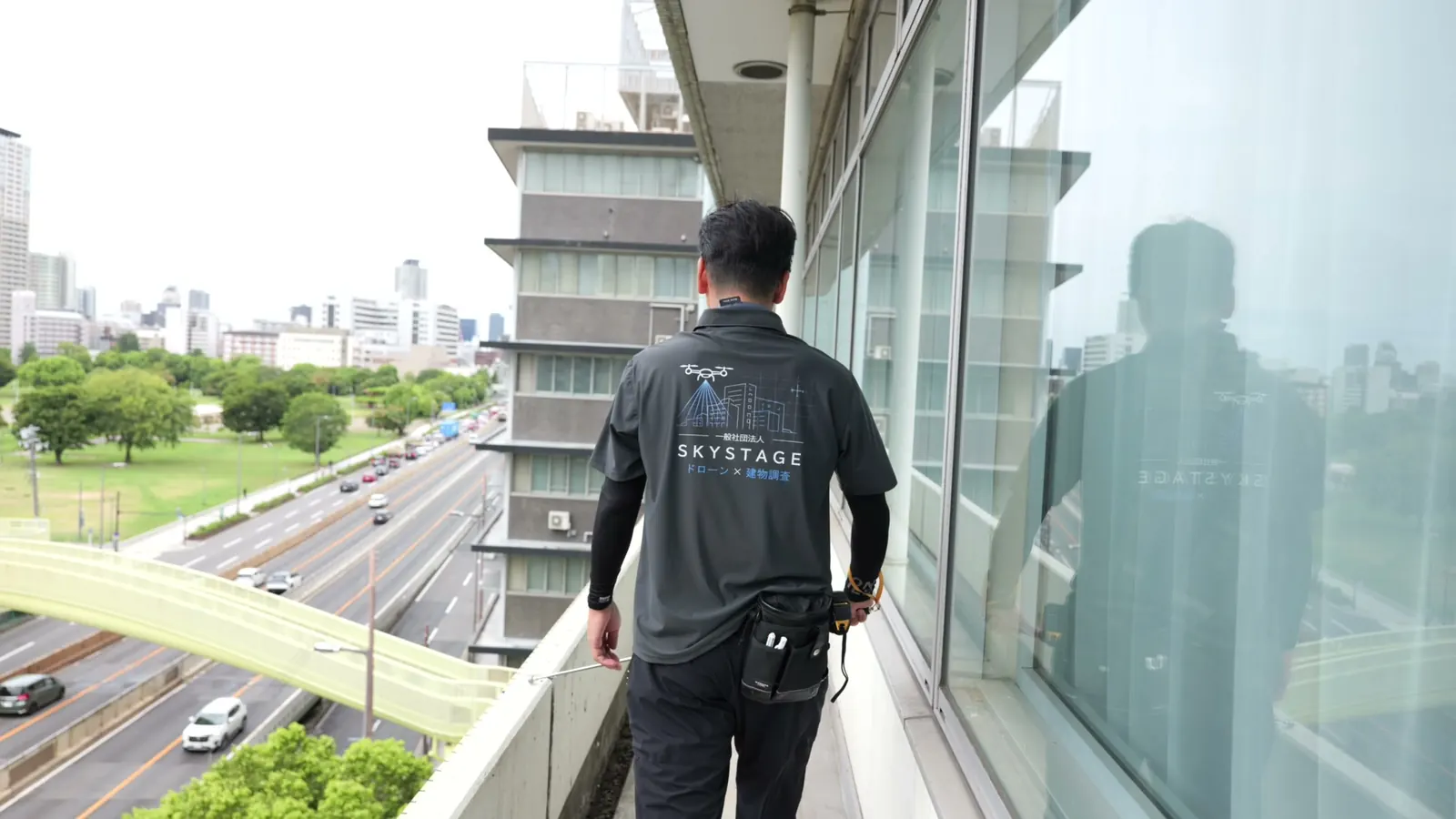 ホテル外部の細い廊下を歩く調査員。下には道路と車が見える