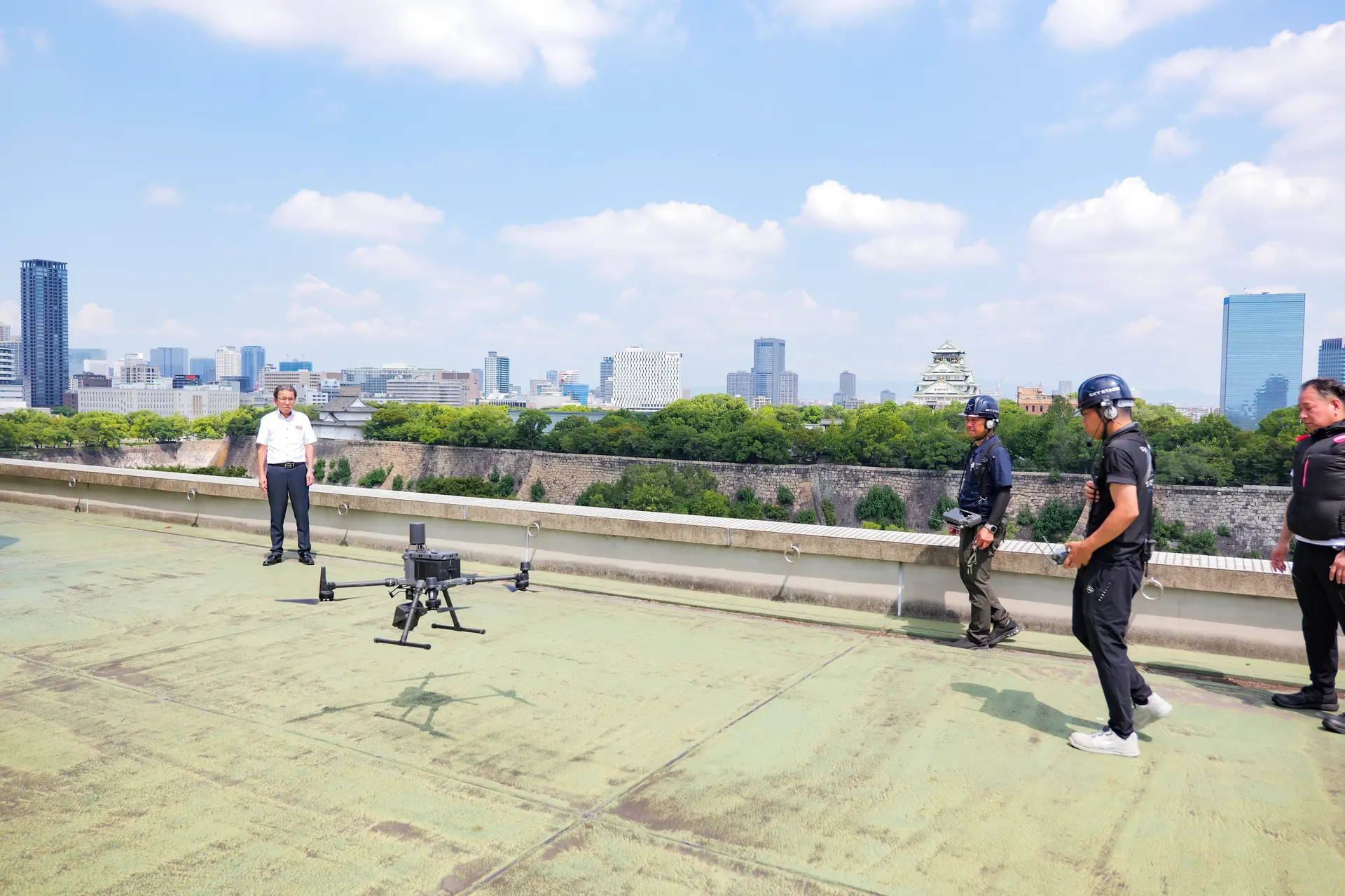 大阪市中央区のホテル屋上。ドローンの前に調査メンバーが立ち、背景に大阪城が見える